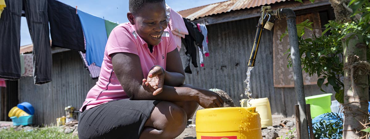 Kvinne fyller vann i gul plasttank
