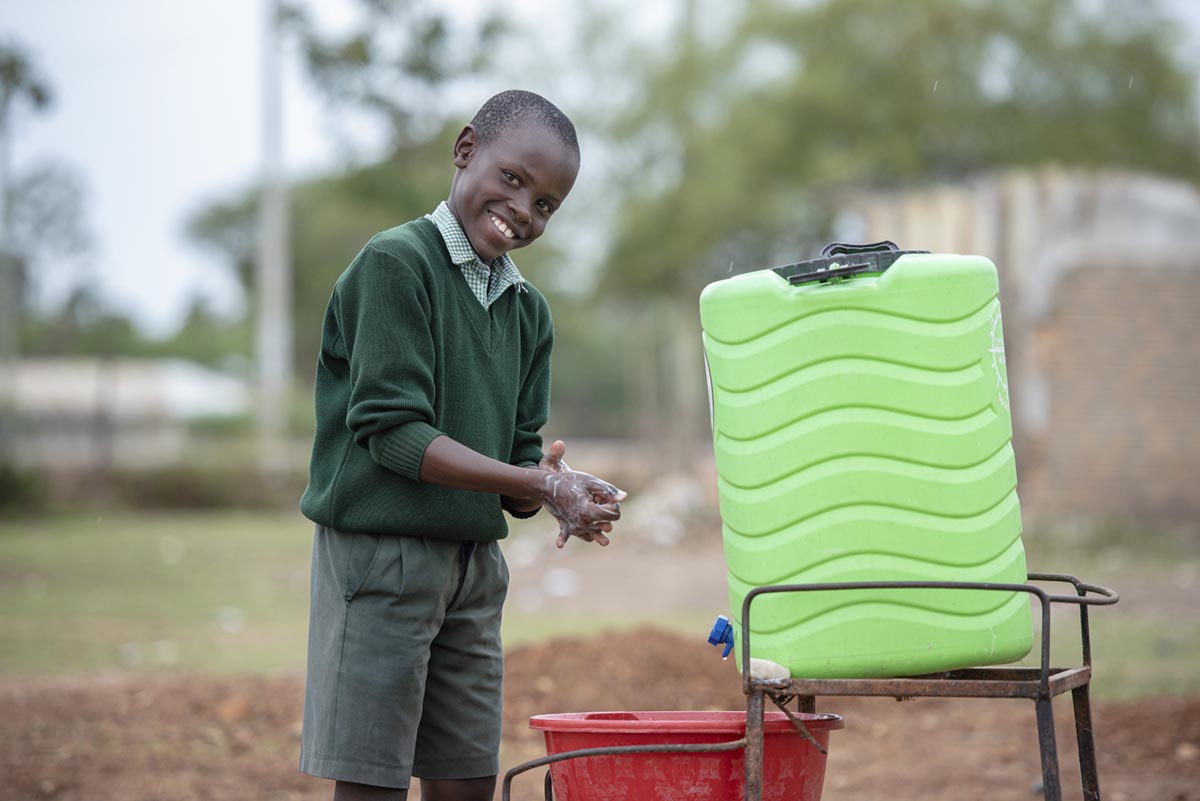 Young boy washing hand close to water tank